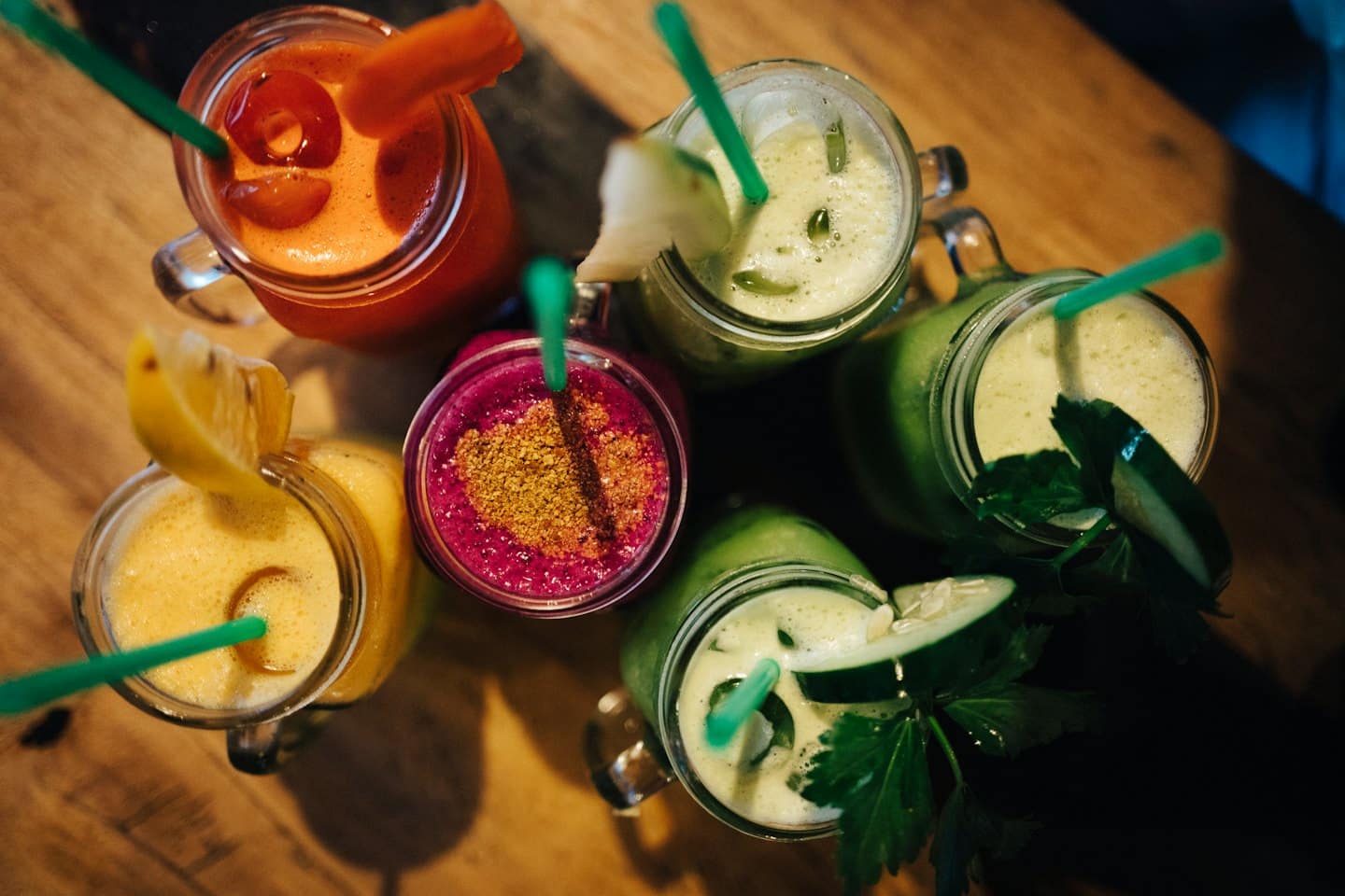 Five colorful fruit smoothies in mason jars on a wooden table.